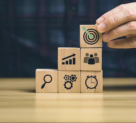 Stacked wooden blocks with icons: target, growth, team, search, gears and clock.